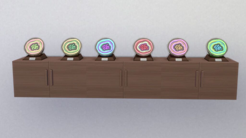 A screenshot from The Sims 4 showing a white wall with cabinets on it. On top of the cabinets are all six items in the geodes collection