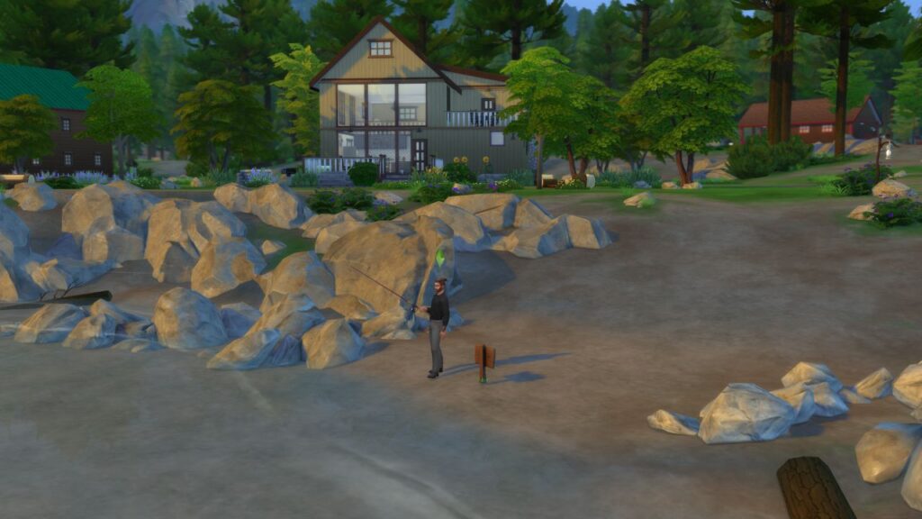 A screenshot from The Sims 4 showing a sim fishing on a beach with rocks around and a large cabin in the background