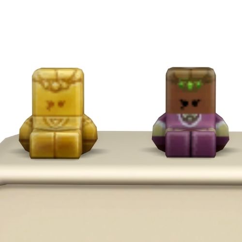 A screenshot from the sims 4 the top of a table with two Simmies on top. The one is gold and the other is a regular Madame Zoe Simmi