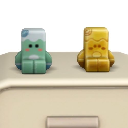 A screenshot from the sims 4 the top of a table with two Simmies on top. The one is gold and the other is a regular Yamachan Simmi