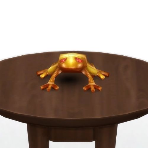 A screenshot from The Sims 4 showing a brown circle table and on top is a golden frog with red eyes