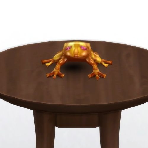 A screenshot from The Sims 4 showing a brown circle table and on top is a golden frog with red eyes