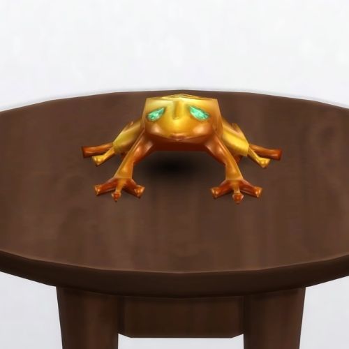 A screenshot from The Sims 4 showing a brown circle table and on top is a golden frog with green eyes